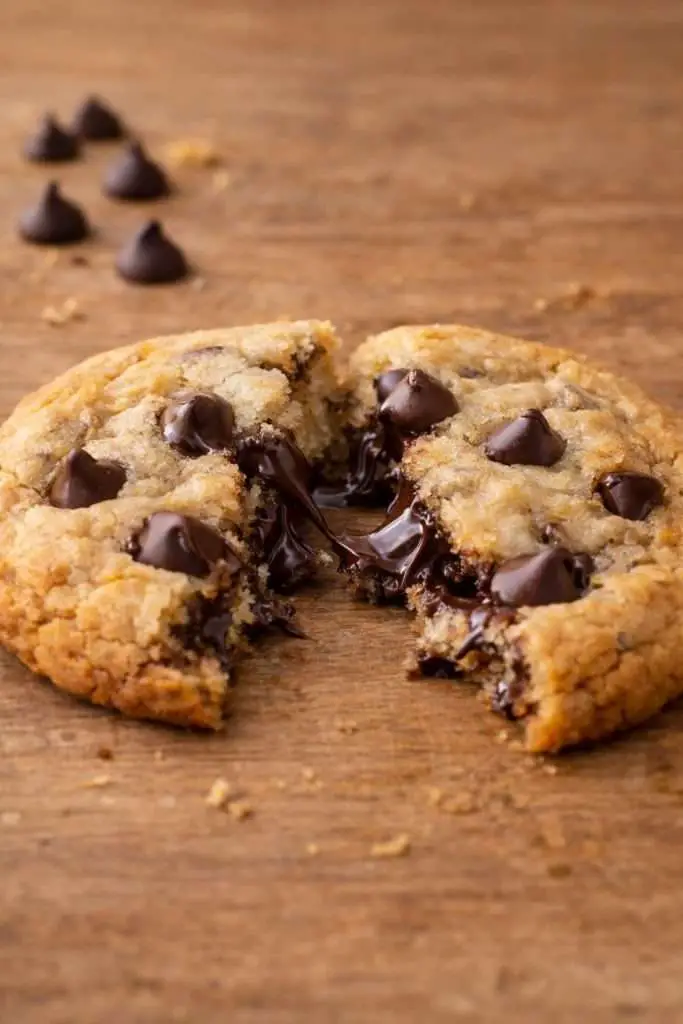 broken homemade chocolate chip cookie showing melted chocolate chips on a wooden surface