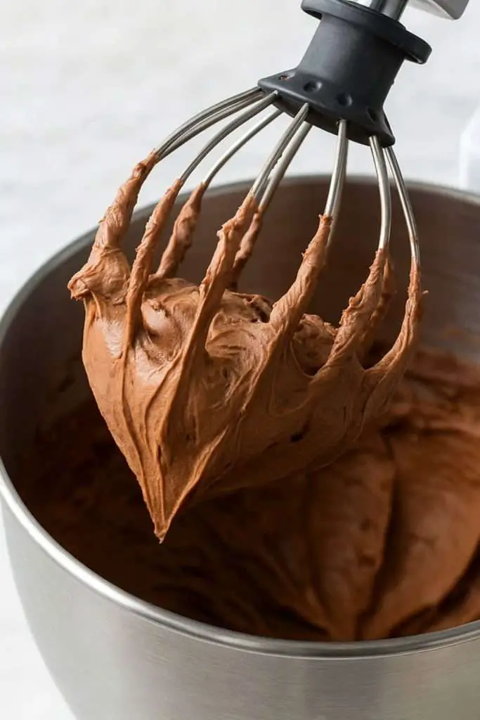 Close-up of fluffy whipped milk chocolate ganache frosting on a stand mixer whisk