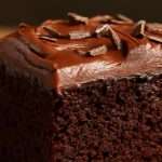 A fudgy squareslice of chocolate cake topped with fluffy old-fashioned chocolate frosting and sprinkled chocolate shreds