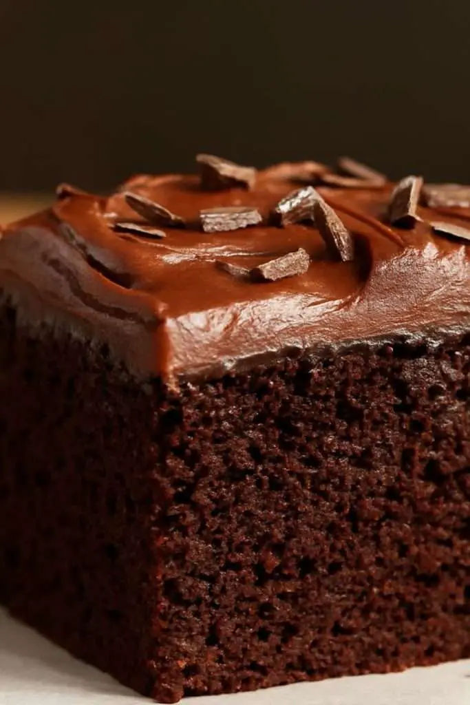 A fudgy squareslice  of chocolate cake topped with fluffy old-fashioned chocolate frosting and sprinkled chocolate shreds