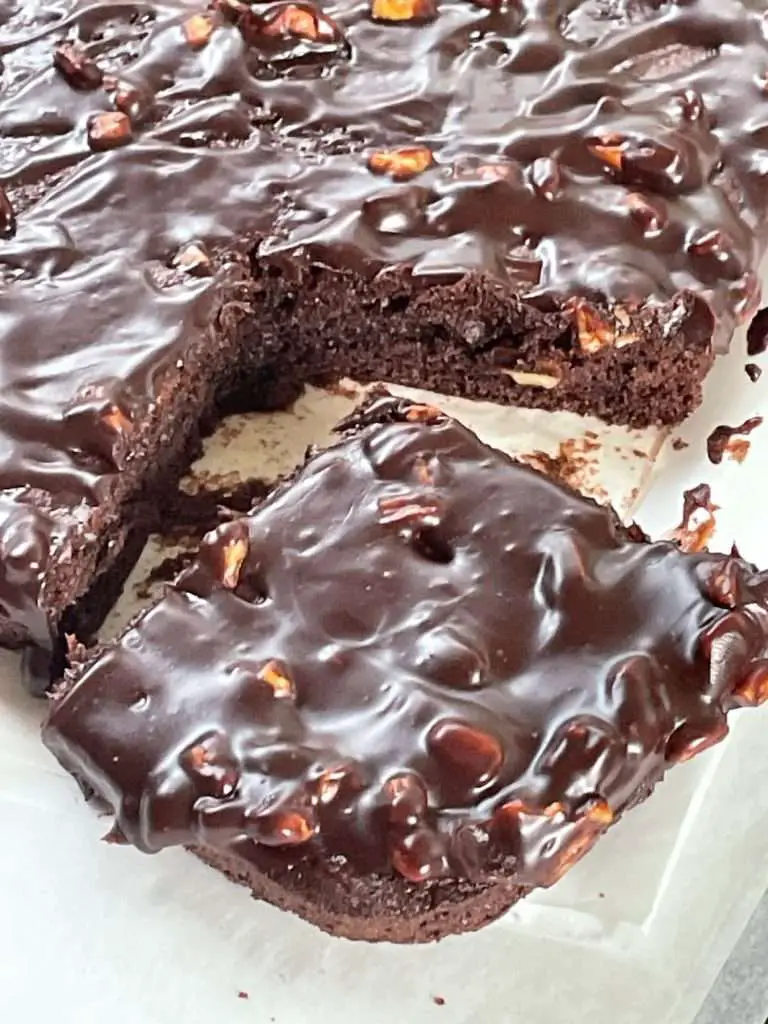 Close-up of a fudgy slice of Texas sheet cake topped with glossy cocoa pecan glaze, pulled from the pan to reveal moist texture inside.