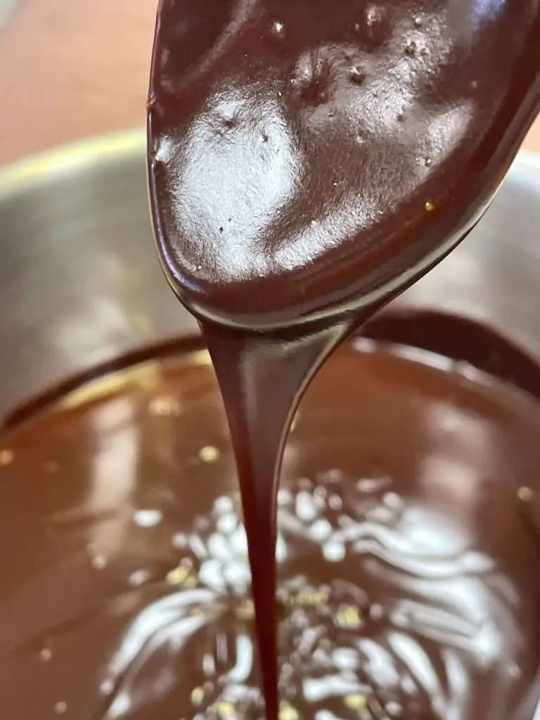Rich, glossy chocolate glaze streaming from a spoon into a mixing bowl, ready to pour over Texas sheet cake.