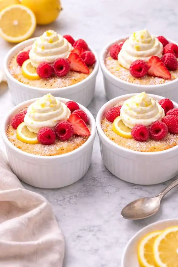 four baked lemon pudding cakes in white ramekins topped with whipped cream and fresh berries (lemon pudding cake recipe)