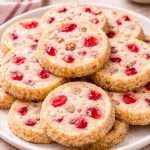cherry icebox cookies stacked on a holiday plate with maraschino cherry pieces and sugar-coated edges