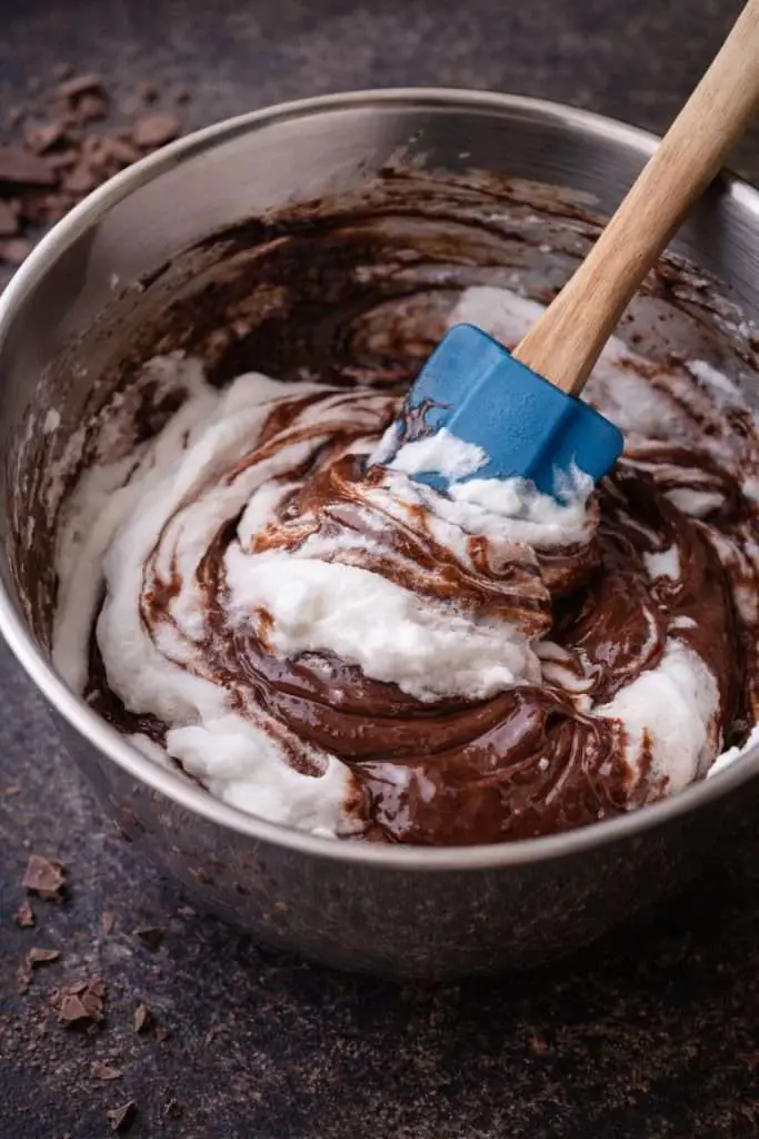 Folding whipped egg whites into melted dark chocolate mixture to make Portuguese chocolate mousse