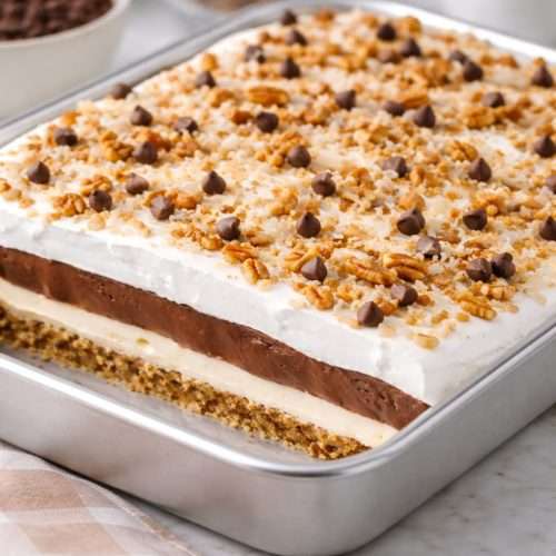 midnight cowboy delight layered chocolate pudding dessert in a baking dish topped with coconut pecans and chocolate chips